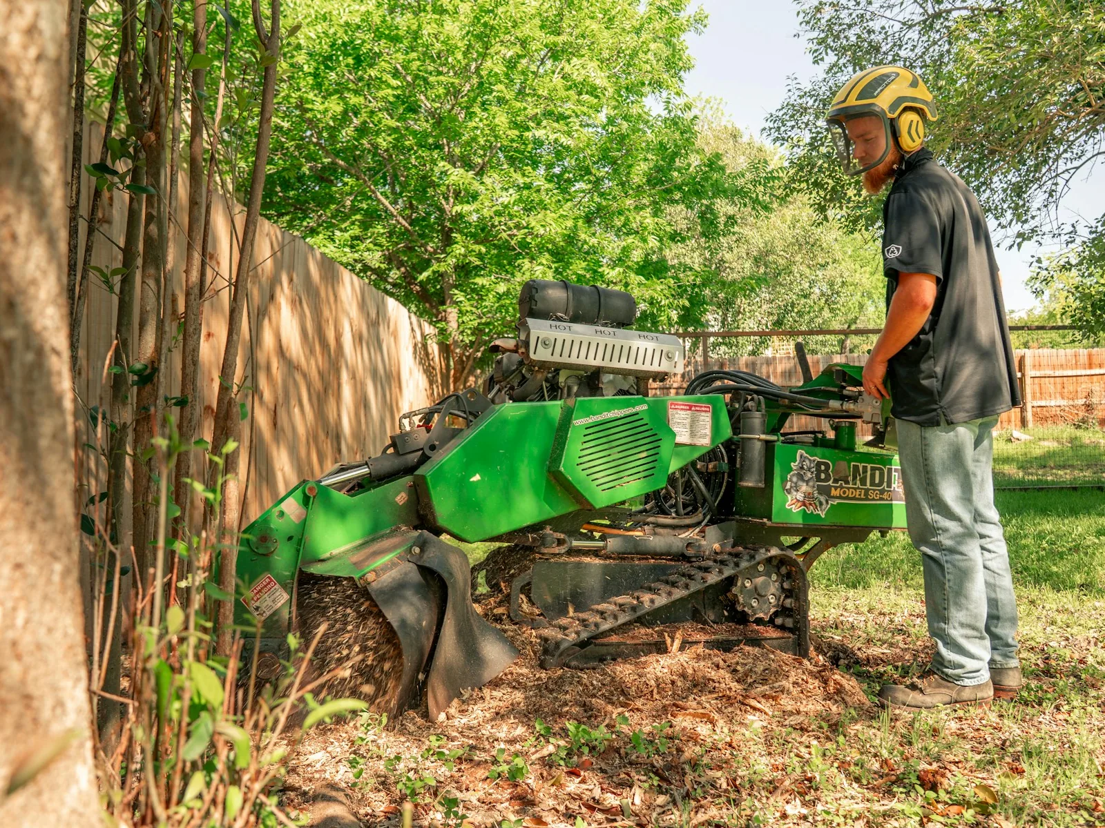 A worker operating a stump grinder on a tree stump
